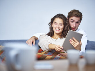 Happy young couple on couch with digital tablet - DISF002255