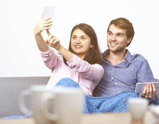 Young couple on couch taking selfie with cell phone - DISF002266