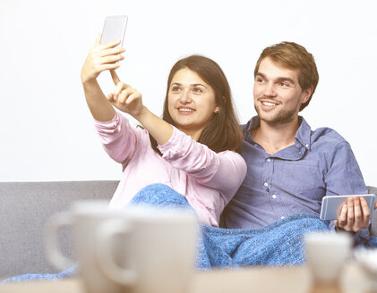 Junges Paar auf Couch nimmt Selfie mit Handy - DISF002266