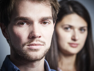 Porträt eines ernsten jungen Mannes mit Freundin im Hintergrund - DISF002267
