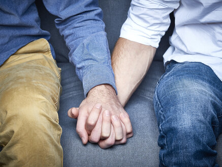 Teilansicht eines homosexuellen Paares, das sich auf einer Couch die Hände hält - DISF002270