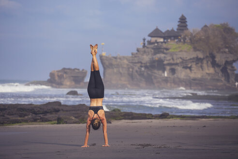 Indonesien, Bali, Tanah Lot, Frau macht einen Handstand am Strand - KNTF000199