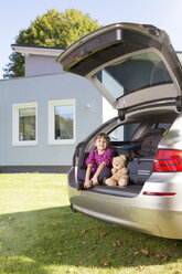 Smiling girl in with teddy bear car boot in front of house - FKF001609