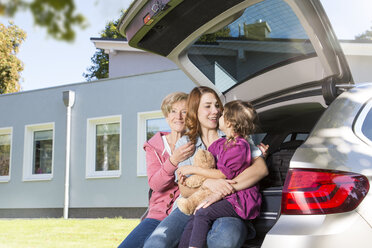 Grandmother, mother and daughter in car boot with teddy bear in front of house - FKF001613