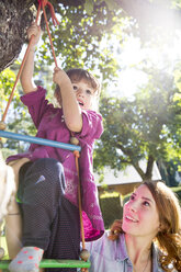Mother watching daughter on rope ladder in garden - FKF001623