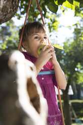 Mädchen isst einen Apfel auf einer Strickleiter im Garten - FKF001627