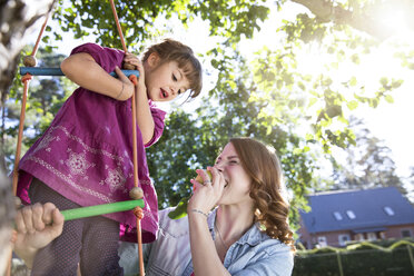 Mutter isst einen Apfel mit Tochter auf Strickleiter im Garten - FKF001628