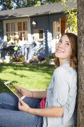 Junge Frau mit digitalem Tablet entspannt sich im Garten - FKF001631