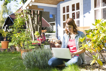 Junge Frau benutzt Laptop im Garten - FKF001633