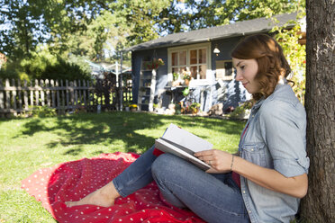 Junge Frau liest ein Buch im Garten - FKF001635