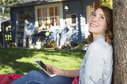 Junge Frau mit digitalem Tablet entspannt sich im Garten, lizenzfreies Stockfoto