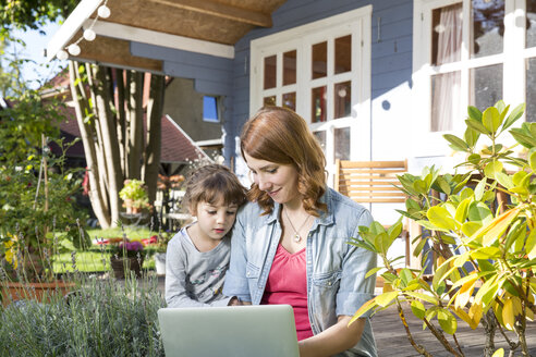 Mutter und Tochter schauen auf der Gartenterrasse auf einen Laptop - FKF001640