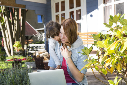 Mutter und Tochter schauen auf der Gartenterrasse auf einen Laptop - FKF001643