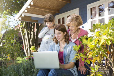 Großmutter, Mutter und Tochter schauen auf der Gartenterrasse auf einen Laptop - FKF001644