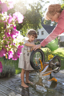 Grandmother and granddaughter washing bicycle on garden terrace - FKF001646