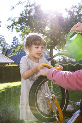 Mädchen und Frau waschen Fahrrad im Garten - FKF001647