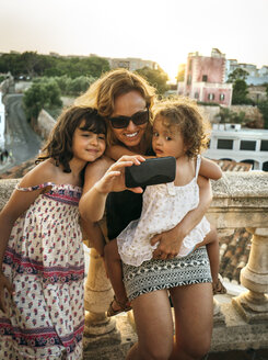 Spanien, Menorca, Frau und ihre kleinen Töchter machen ein Selfie mit Smartphone - MGOF001118