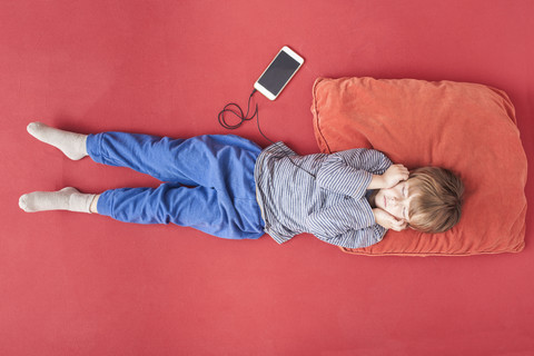 Little boy lying on bed hearing music with smartphone and earphones stock photo