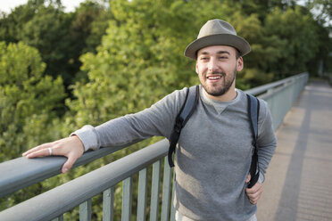 Portrait of bearded young man wearing hat standing on a bridge - PAF001496