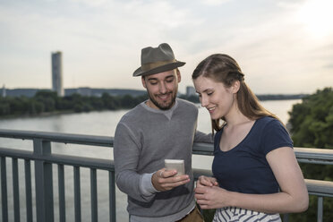 Deutschland, Bonn, junges Paar steht auf der Rheinbrücke und schaut auf sein Smartphone - PAF001497