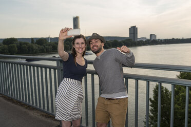 Germany, Bonn, young couple standing on Rhine bridge taking a selfie with smartphone - PAF001498