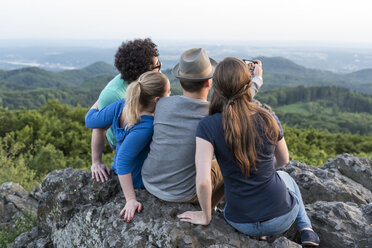 Germany, Siebengebirge, back view of four friends taking a selfie with smartphone on Mount Olivet - PAF001500