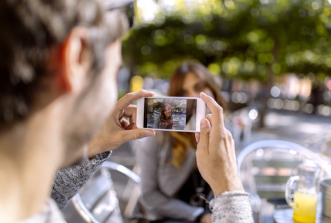 Junger Mann fotografiert seine Freundin mit dem Smartphone, lizenzfreies Stockfoto