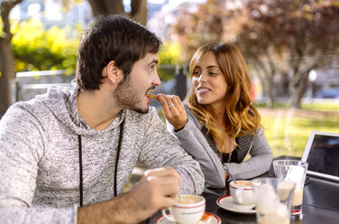 Young woman feeding her boyfriend in a sidewalk cafe - MGOF001125