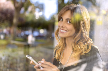 Portrait of smiling young woman with smartphone - MGOF001130
