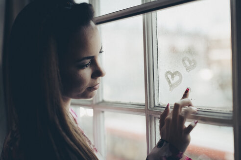 Young woman drawing hearts on fogged-up windowpane - MAUF000131