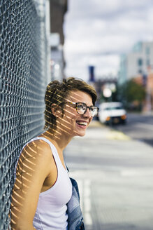 USA, New York City, Williamsburg, portrait of happy blond woman leaning against wire fence - GIOF000553