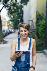 Happy blond woman wearing jeans dungarees with smartphone - GIOF000569