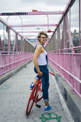 USA, New York City, Williamsburg, smiling woman with red racing cycle on Williamsburg Bridge - GIOF000581