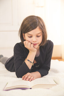 Portrait of girl lying on blanket on the floor reading a book - LVF004227