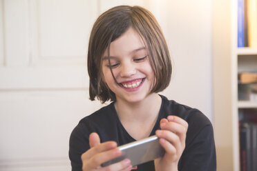 Porträt eines lächelnden Mädchens mit Blick auf ein Smartphone - LVF004232