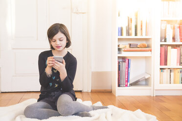 Porträt eines Mädchens, das auf einer Decke auf dem Boden sitzt und ein Smartphone benutzt - LVF004234