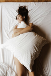 Daydreaming woman lying on bed covering her body with a pillow - GEMF000533