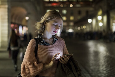 UK, London, young woman using smartphone on the street in the evening - MAUF000133