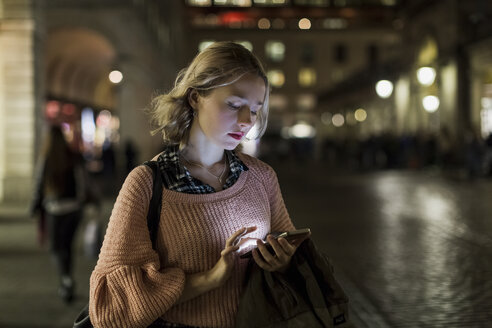 UK, London, junge Frau, die abends auf der Straße ihr Smartphone benutzt - MAUF000133