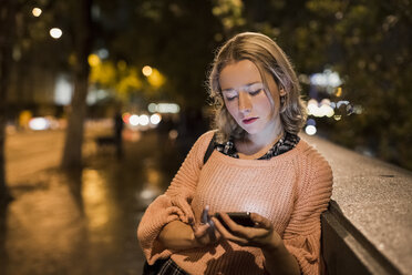 UK, London, junge Frau benutzt ihr Smartphone auf der Straße am Abend - MAUF000137