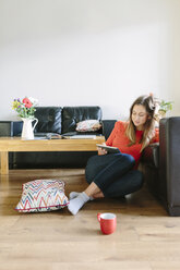 Young woman sitting on the floor of her living room looking at digital tablet - BOYF000018