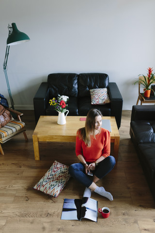 Young woman sitting on the floor of her living room relaxing stock photo