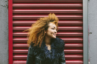 Irland, Dublin, lächelnde Frau mit Afro vor rotem Rolltor - BOYF000031