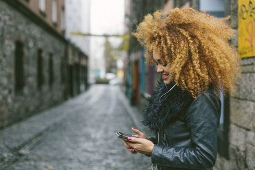 Ireland, Dublin, smiling woman with afro looking at her smartphone - BOYF000033