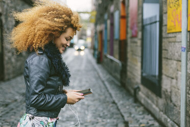 Irland, Dublin, lächelnde Frau mit Afro, die auf ihr Smartphone schaut - BOYF000034