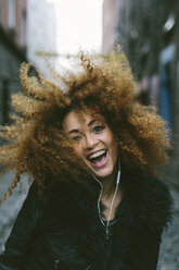 Porträt einer glücklichen Frau mit Afro, die mit Kopfhörern Musik hört - BOYF000038