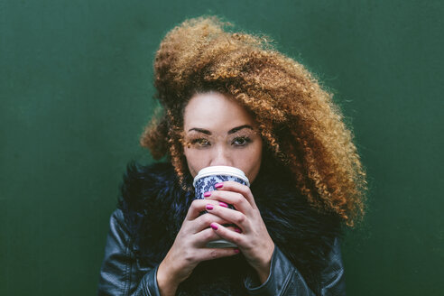 Portrait of woman drinking coffee to go in front of a green wall - BOYF000043