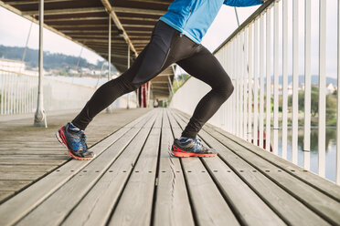 Spain, Naron, legs of a jogger stretching on a wooden bridge - RAEF000701