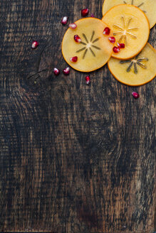 Kaki-Scheiben und Granatapfelkerne auf dunklem Holz - SBDF002505