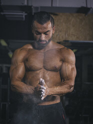 Bodybuilder chalking his hands in gym - MADF000764